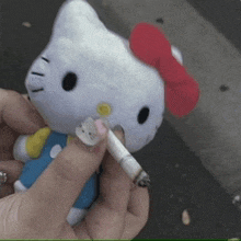 a person is holding a stuffed hello kitty and a cigarette in their hand