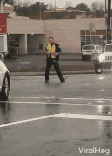 a man in a safety vest is walking across a street in the rain with the words viralhog below him