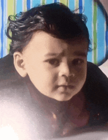 a baby with curly hair looks at the camera with a striped background