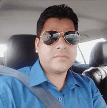 a man wearing sunglasses and a blue shirt is sitting in the driver 's seat of a car