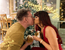 a man and woman kissing in front of a christmas tree with the words happy holidays written in yellow