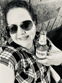 a woman wearing sunglasses holds a bottle of modelo beer