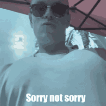 a man wearing sunglasses stands under an umbrella with the words sorry not sorry below him