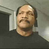 a man with a mustache wearing a black shirt is standing in a hallway