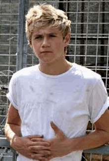 a young man in a white t-shirt is standing in front of a fence .