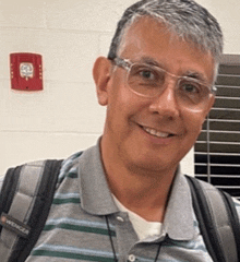 a man wearing glasses and a backpack smiles for the camera