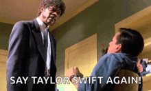 a man in a suit and tie is standing next to another man in a chair and saying " say taylor swift again " .