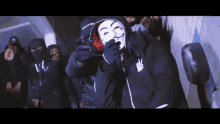 a man wearing a mask holds a gun in front of a group of masked people