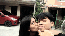 a woman kissing a man in front of a red car