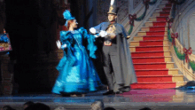 a man in a top hat and a woman in a blue dress are dancing on a stage