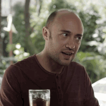 a man in a brown shirt is sitting at a table with a glass of beer in front of him