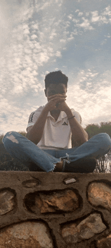 a man wearing an adidas shirt sits on a rock wall