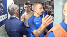 a group of soccer players are standing in a locker room with a man in a suit talking to them .