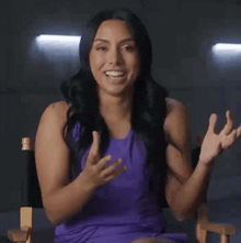 a woman in a purple dress is sitting in a director 's chair clapping her hands .