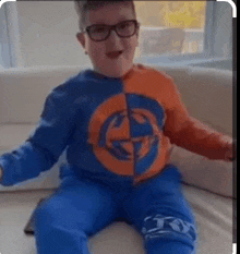 a young boy wearing glasses is sitting on a couch wearing a blue and orange shirt .