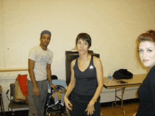 a woman in a black adidas tank top stands in a room with other people