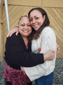two women hugging each other in front of a yellow wall
