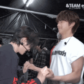 a man wearing a white shirt with the word team on it is holding another man 's hand