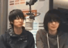 two men are sitting next to each other in front of a microphone .