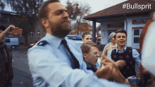 a man in a police uniform stands in front of a group of people with #bullsprit written on the bottom right