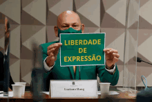 a man in a green suit holds a sign that says liberdade de expressao