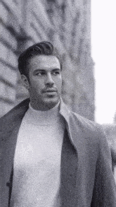 a black and white photo of a man wearing a white turtleneck and a coat .