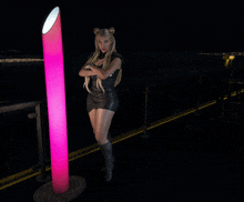 a woman in a black dress stands next to a pink light pole