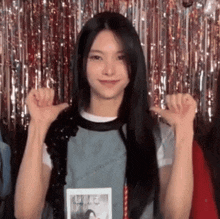 a young woman with long black hair is giving a thumbs up sign in front of a tinsel curtain .