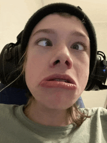 a young girl wearing headphones and a beanie makes a funny face