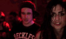 a woman is dancing in a dark room with a man in the background wearing a black shirt that says reck .