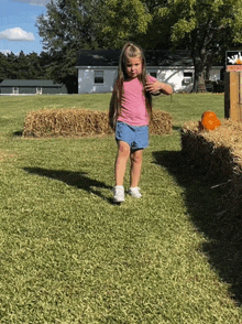 a little girl in a pink shirt and shorts stands in a grassy field