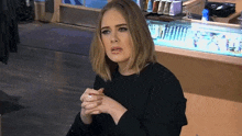 a woman in a black shirt is sitting in front of a counter with her hands folded .