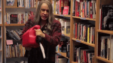 a woman is holding a red gas can in front of a bookshelf with a book titled taking risks on it