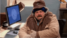 a man wearing a hat and gloves is sitting in front of a computer monitor