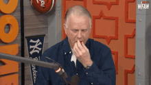 a man in a blue shirt is eating something in front of a microphone with a ny yankees banner behind him