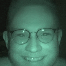 a man wearing glasses is smiling in a dark room .