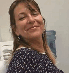 a woman is smiling and looking at the camera while wearing a blue shirt and earrings .