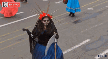 a woman in a grim reaper costume is walking down a street in front of a sign that says en vivo