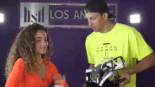 a man in a neon yellow fatal error shirt holds a helmet in front of a sign that says los angeles