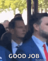 a man in a suit and tie says good job in front of a crowd of people