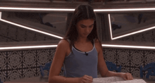 a woman in a blue tank top sits in front of a mirror