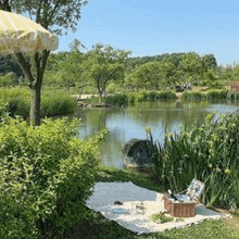 a picnic blanket is sitting on the grass next to a lake with a basket and umbrella .