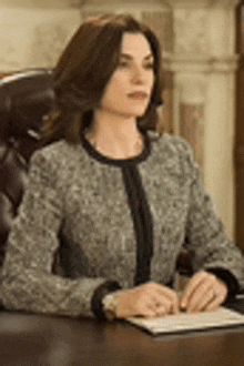 a woman in a suit is sitting at a desk with a pen in her hand .