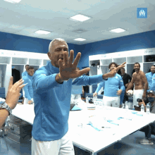 a man in a blue shirt is standing in a locker room with a sign that says olympique de marseille