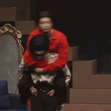 a man in a red jacket is carrying another man on his shoulders in front of a mirror