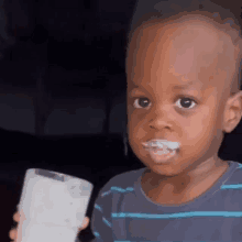 a little boy is holding a glass of milk in his hand and making a funny face .