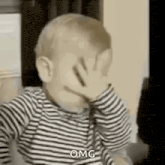 a baby is covering his face with his hand and making a funny face .