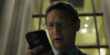 a man wearing glasses is looking at his phone .