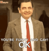 mr bean is wearing a suit and tie and smiling while saying `` you 're funny and gay ok '' .
