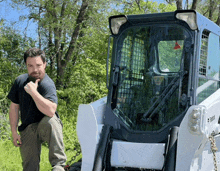 a man kneeling next to a bobcat tractor